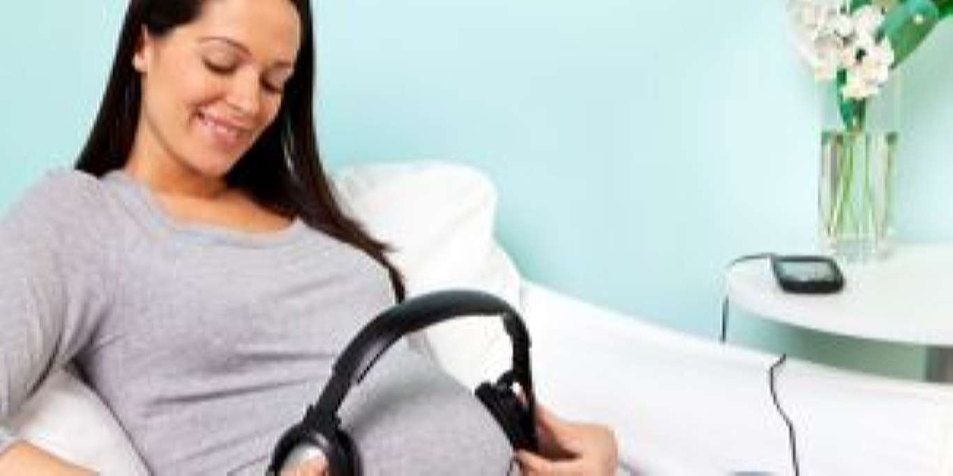 Pregnant woman playing music to her baby through headphones